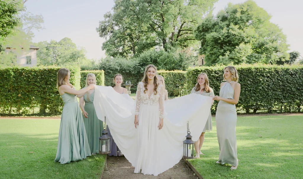 Die Bridal Party präsentiert den langen Schleier der Braut im grünen Park der Villa.