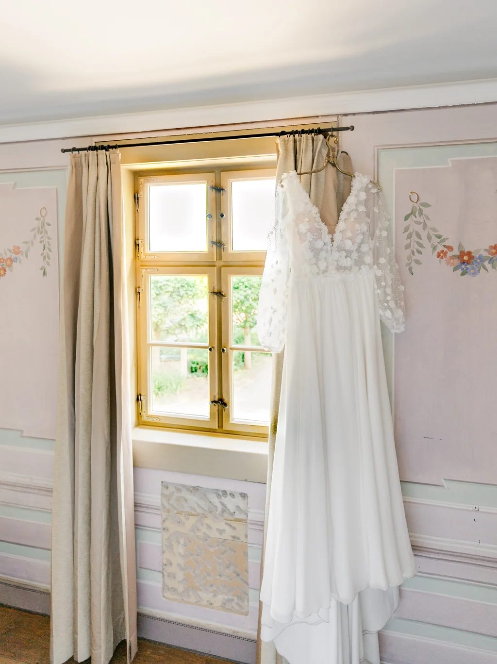 Das weiße Hochzeitskleid hängt bereit für das Getting Ready am Fenster der Villa Sorgenfrei.