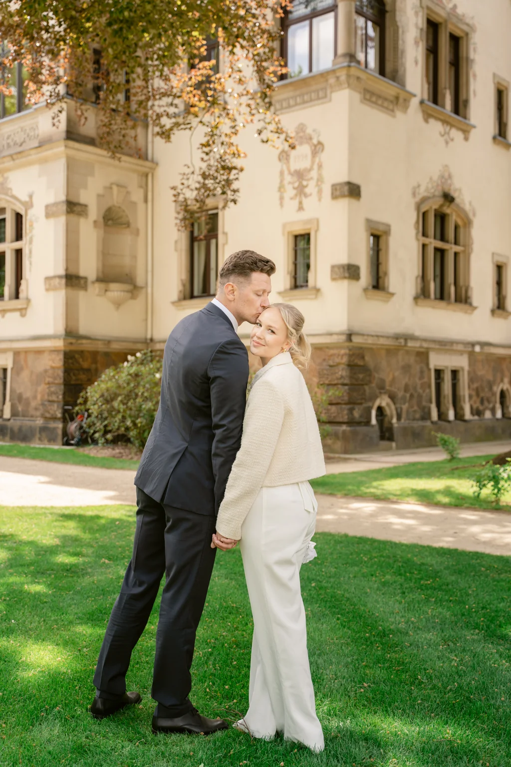 Das Paar steht Hand in Hand vor der prachtvollen, historischen Fassade der Villa Weigang in Dresden.