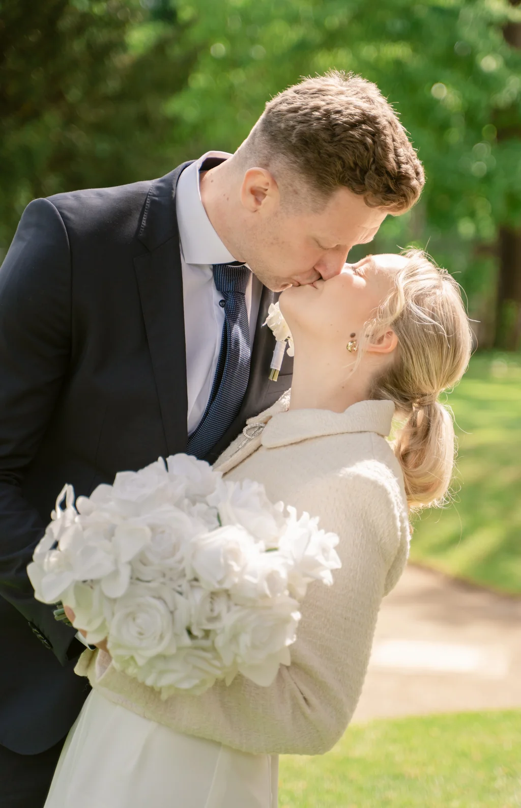 Romantischer Kuss im Park der Goetheallee: Die Braut hält ihren weißen Strauß aus Pfingstrosen in den Händen.