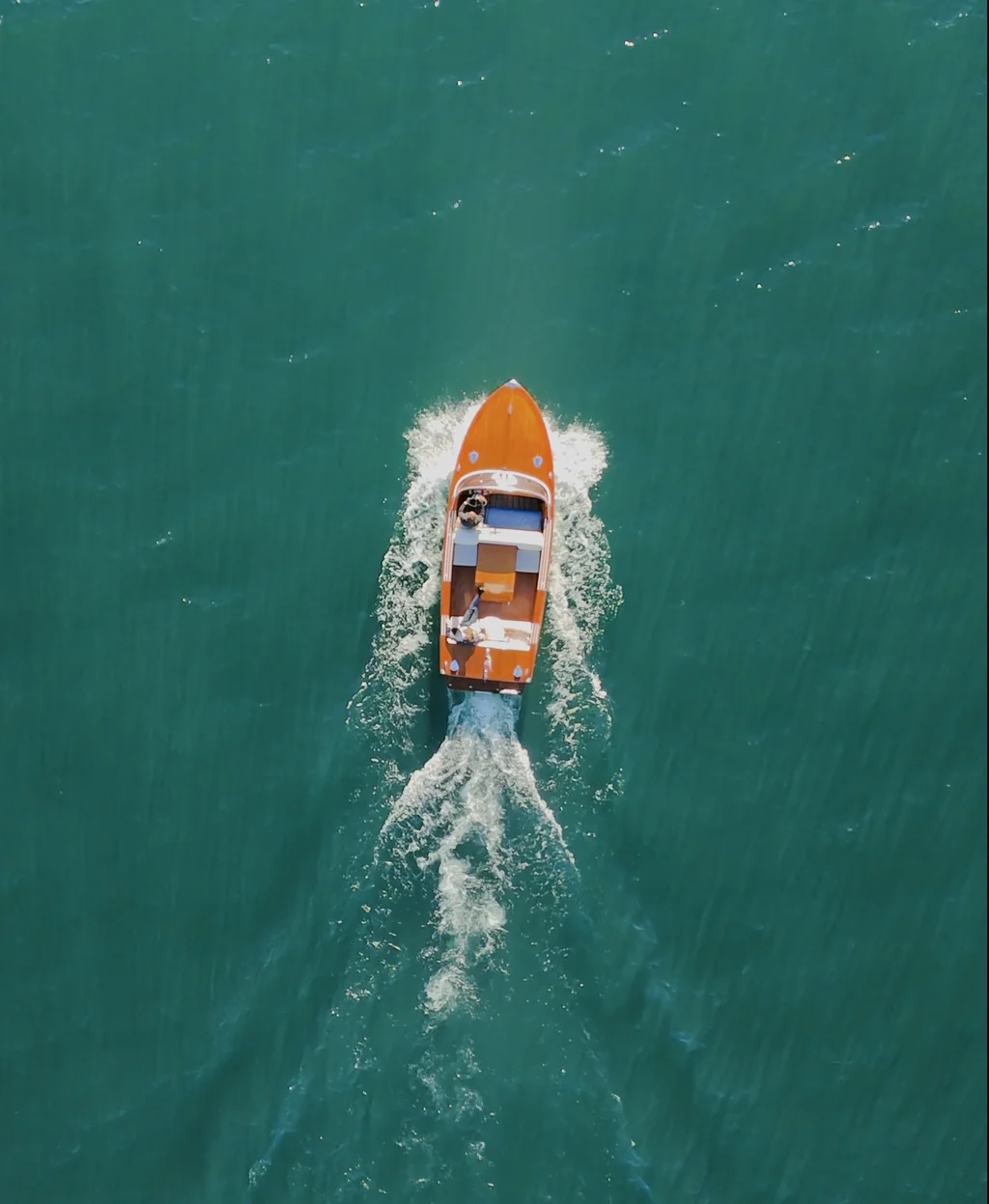Senkrechte Luftaufnahme eines Runabout-Bootes auf dem türkisfarbenen Gardasee.