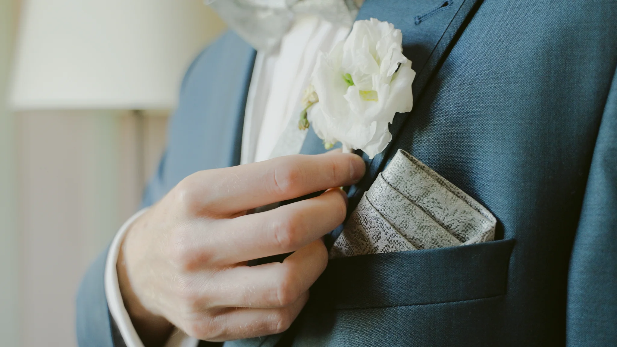 Nahaufnahme vom Bräutigam, der seine weiße Ansteckblume am Revers richtet.