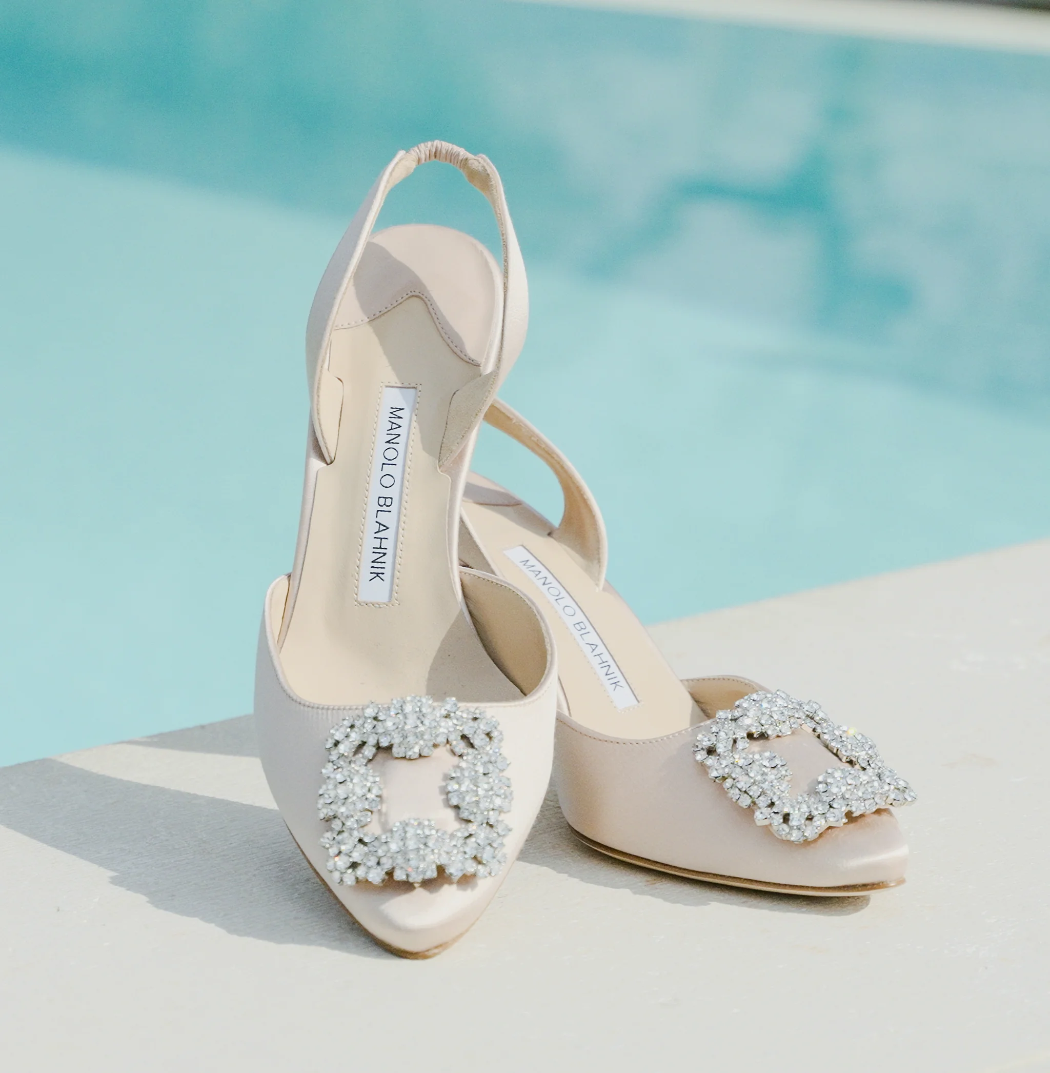 Elegante beige Brautschuhe mit Schnalle stehen am Rand eines Swimmingpools.