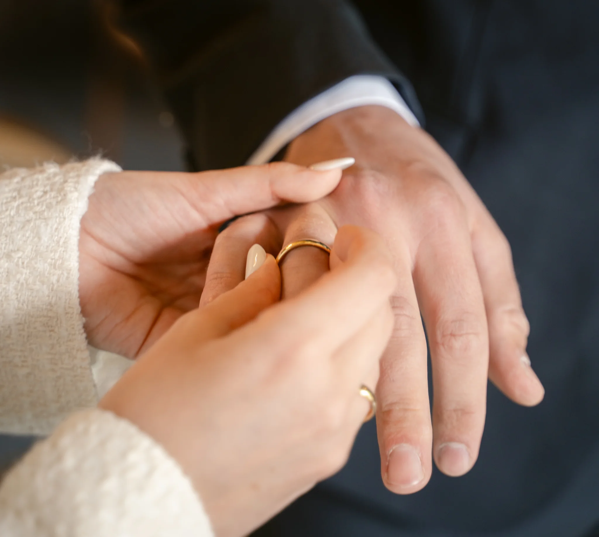 Nahaufnahme der Hände: Die Braut steckt dem Bräutigam den goldenen Ring im hellen Saal der Goetheallee an.
