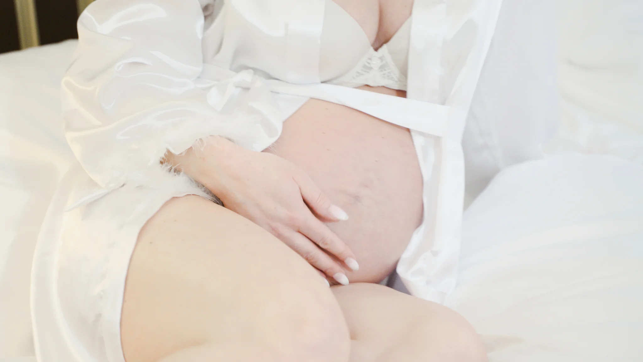 Eine innige Nahaufnahme des runden Babybauchs der Braut im weißen Morgenmantel im Hotel Bülow Palais, in Vorfreude auf die Feier in der Villa Weigang.